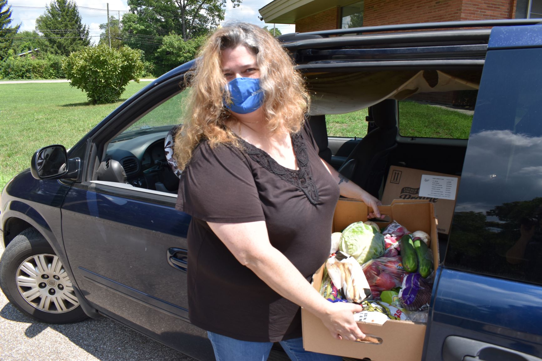 Maria poses with a box filled with fresh vegetables