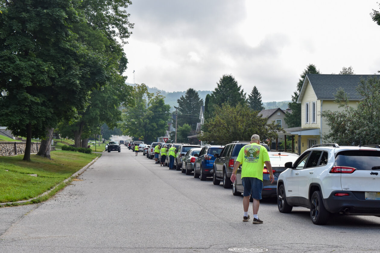Cars line up on a neighborhood street as volunteers sign them in.