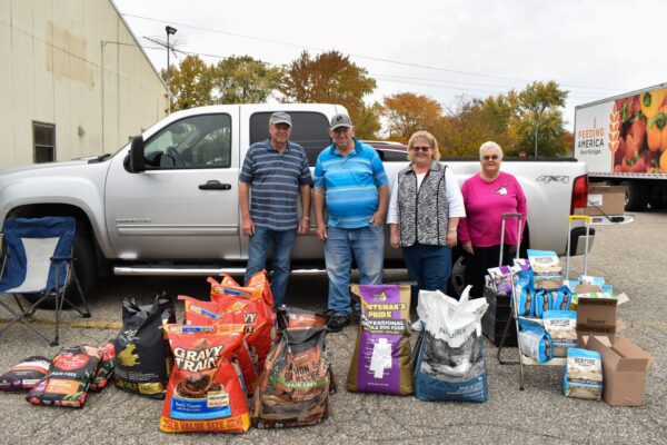 Four volunteers stand behind bags of dog and cat food