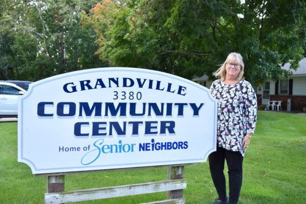 Sherri (Coordinator) smiles while standing by the Grandville Senior Neighbors sign