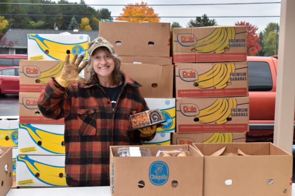 Donna smiles while waving at the camera as she packs food into boxes