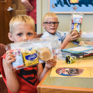 Two kids holding up packs of food from Gather 2 Grow