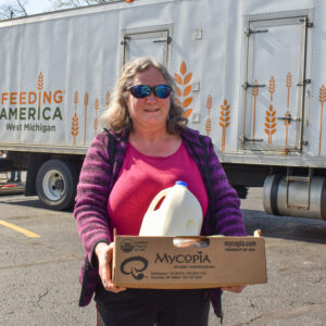 Mary smiling while holding a box of food in front of the Mobile Pantry