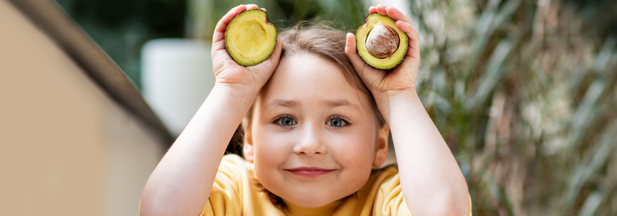 girl holding a sliced avocado on each hand, above her head
