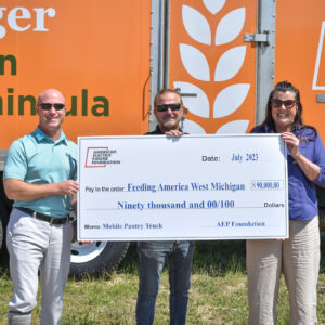 Tres individuos sosteniendo un cheque por noventa mil dólares frente al nuevo camión Mobile Pantry