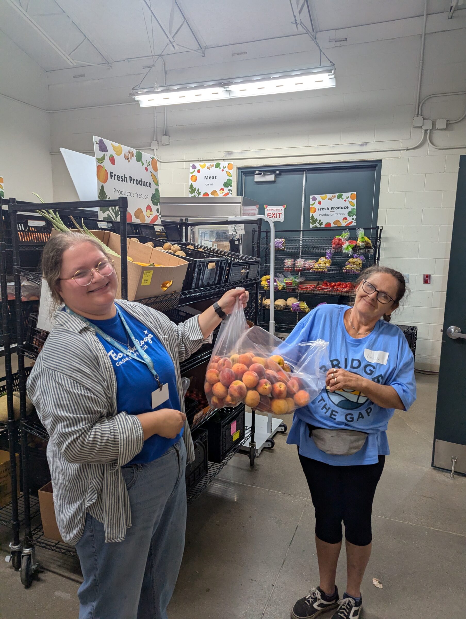 Two women smiling while holding a bag of fruit. 