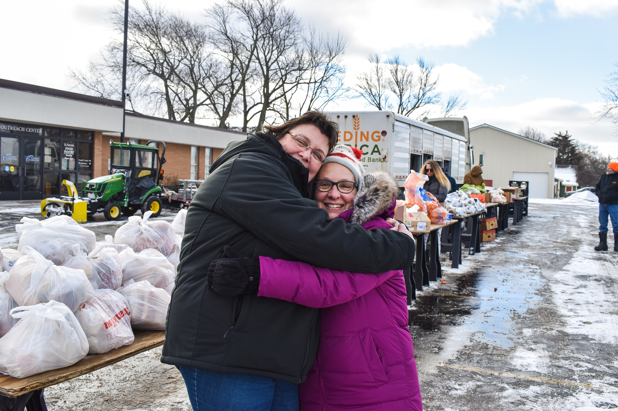 Two women smiling and hugging at a mobile food pantry in winter.