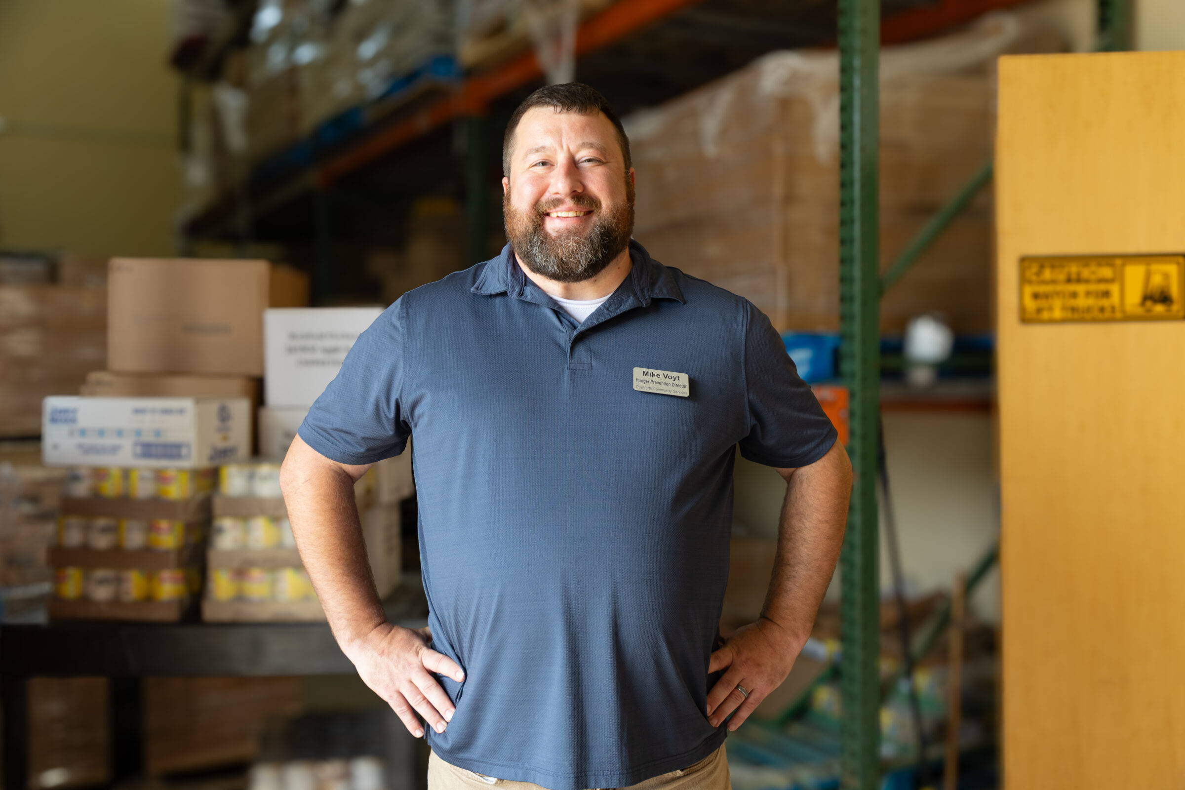 A man with his hands on his hips smiling in a warehouse. 