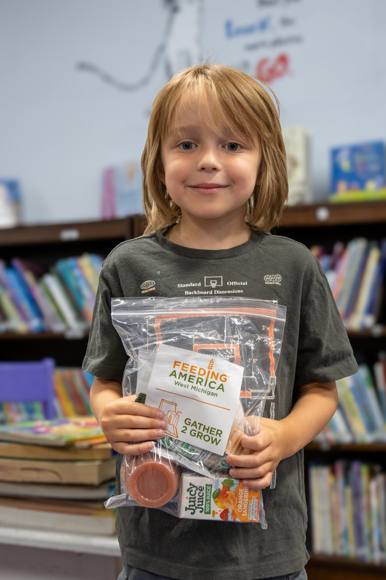 A boy smiling and hold a bag holding a Gather 2 Grow summer meal.