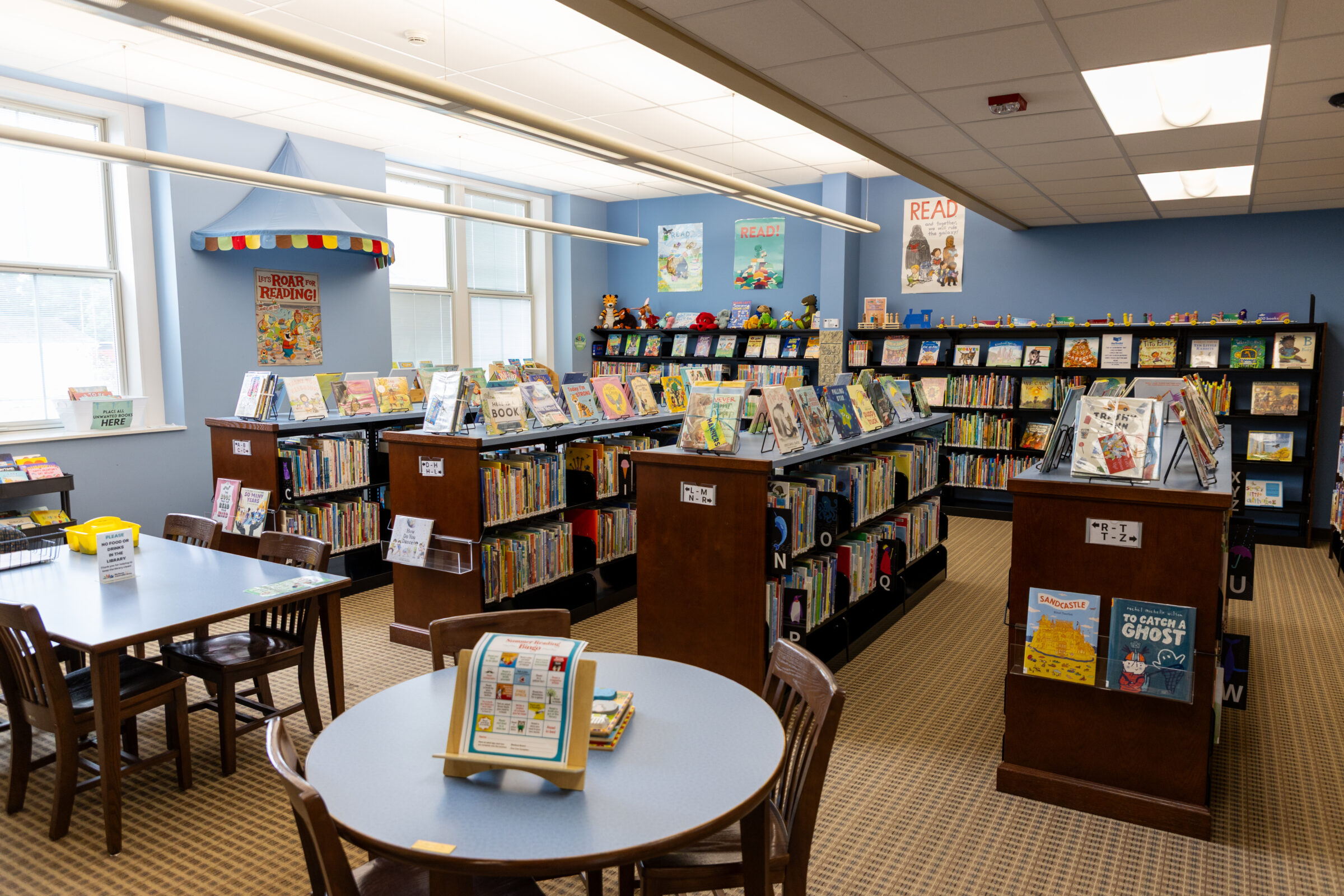 Colorful children’s reading area at Big Rapids Community Library with tables for reading and several shelves of books. 