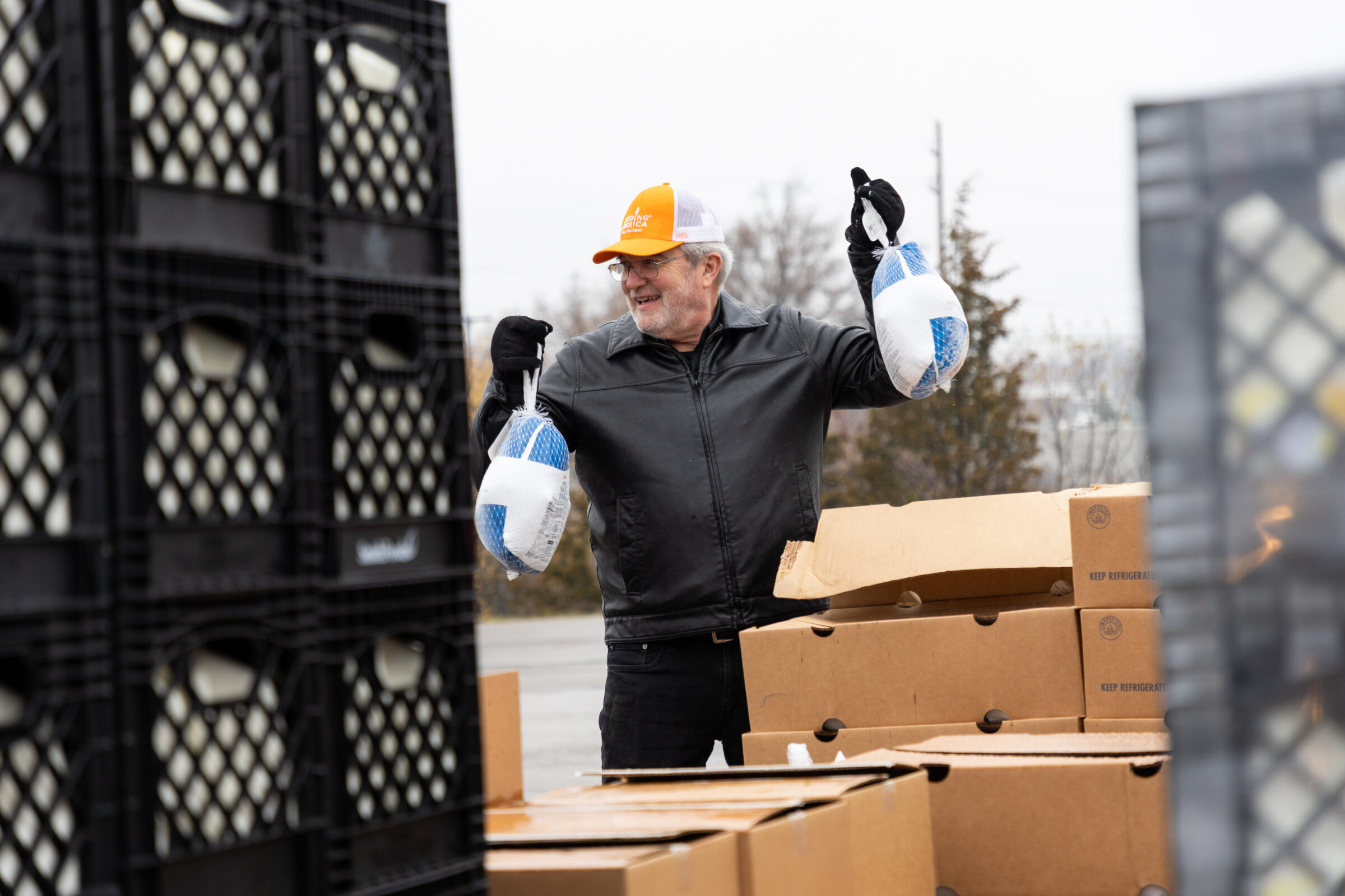 Feeding America West Michigan CEO and president Ken Estelle lifting frozen turkeys while surrounded by crates and boxes at a holiday mobile food pantry. 