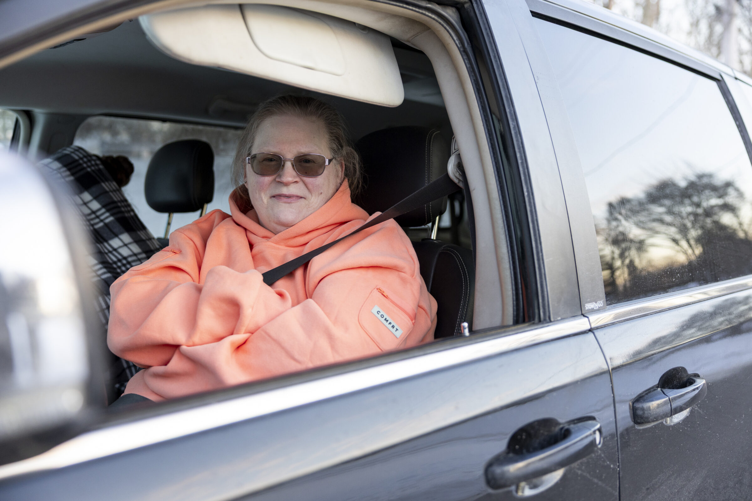 Ionia County mother smiling in her car as she waits in line at a mobile food pantry in winter. 