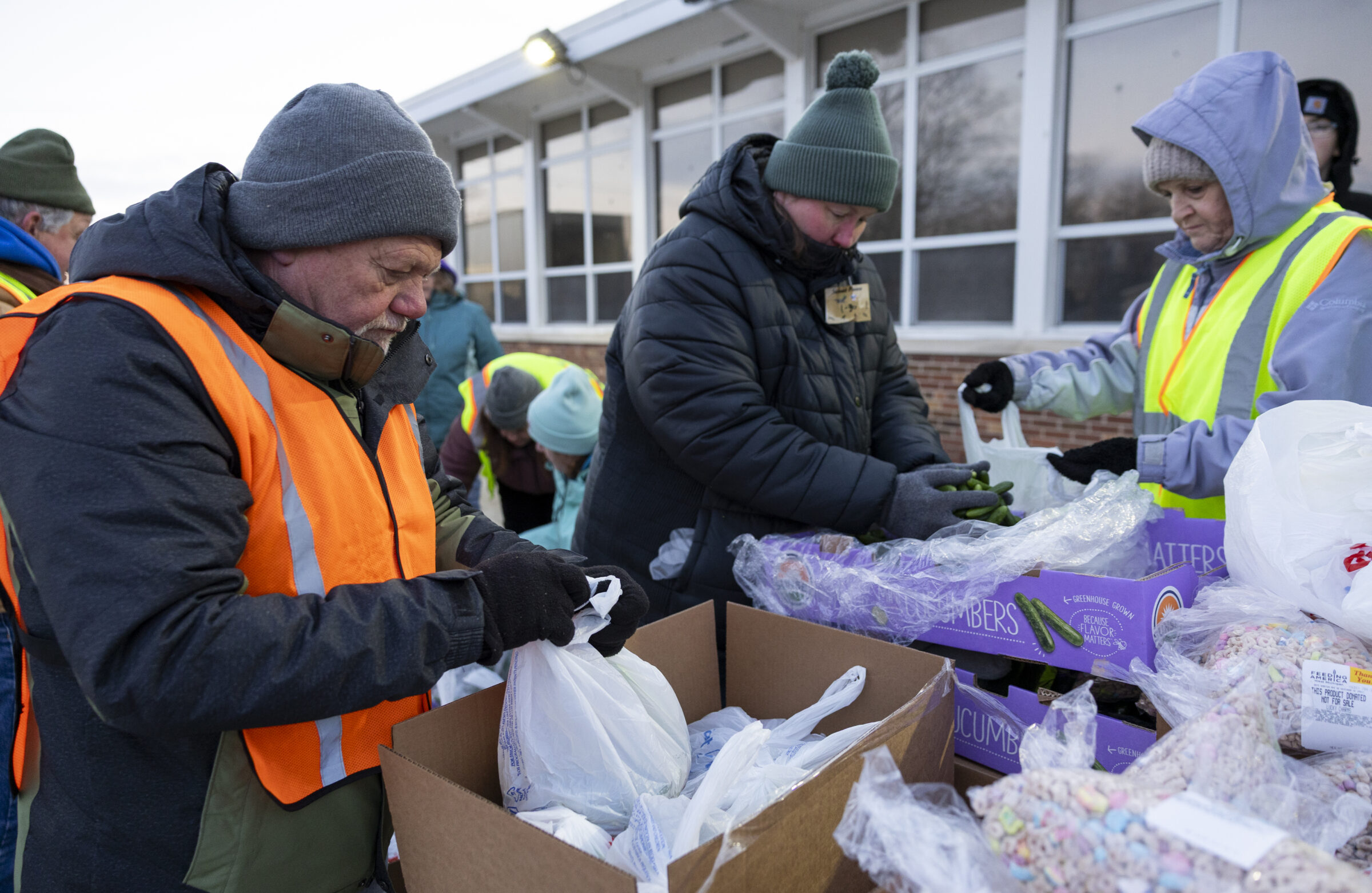 Volunteers in winter gear sorting food items into bags to be loaded in neighbors' cars. 