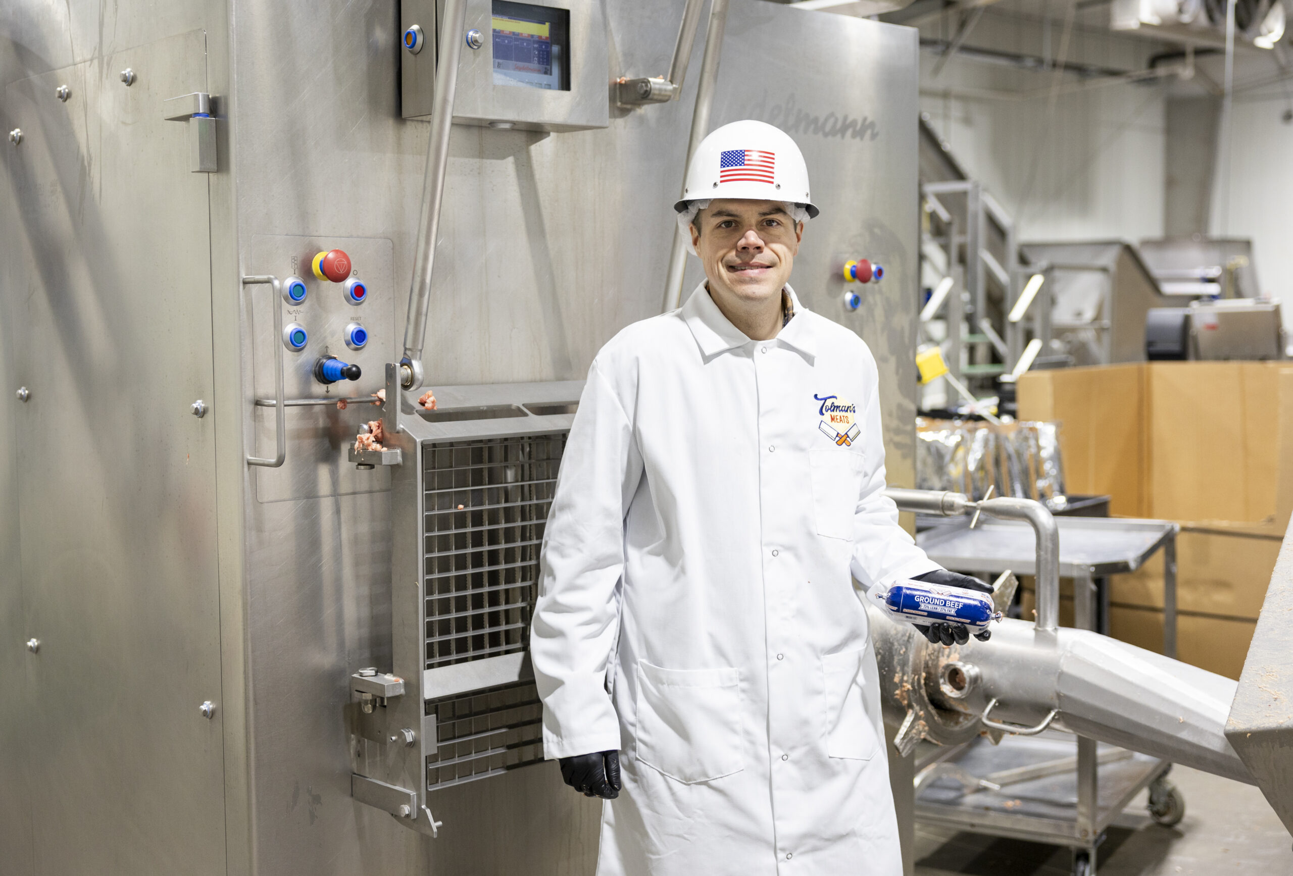 Brandon Bassett of Tolman's Meats smiling in front of a machine.