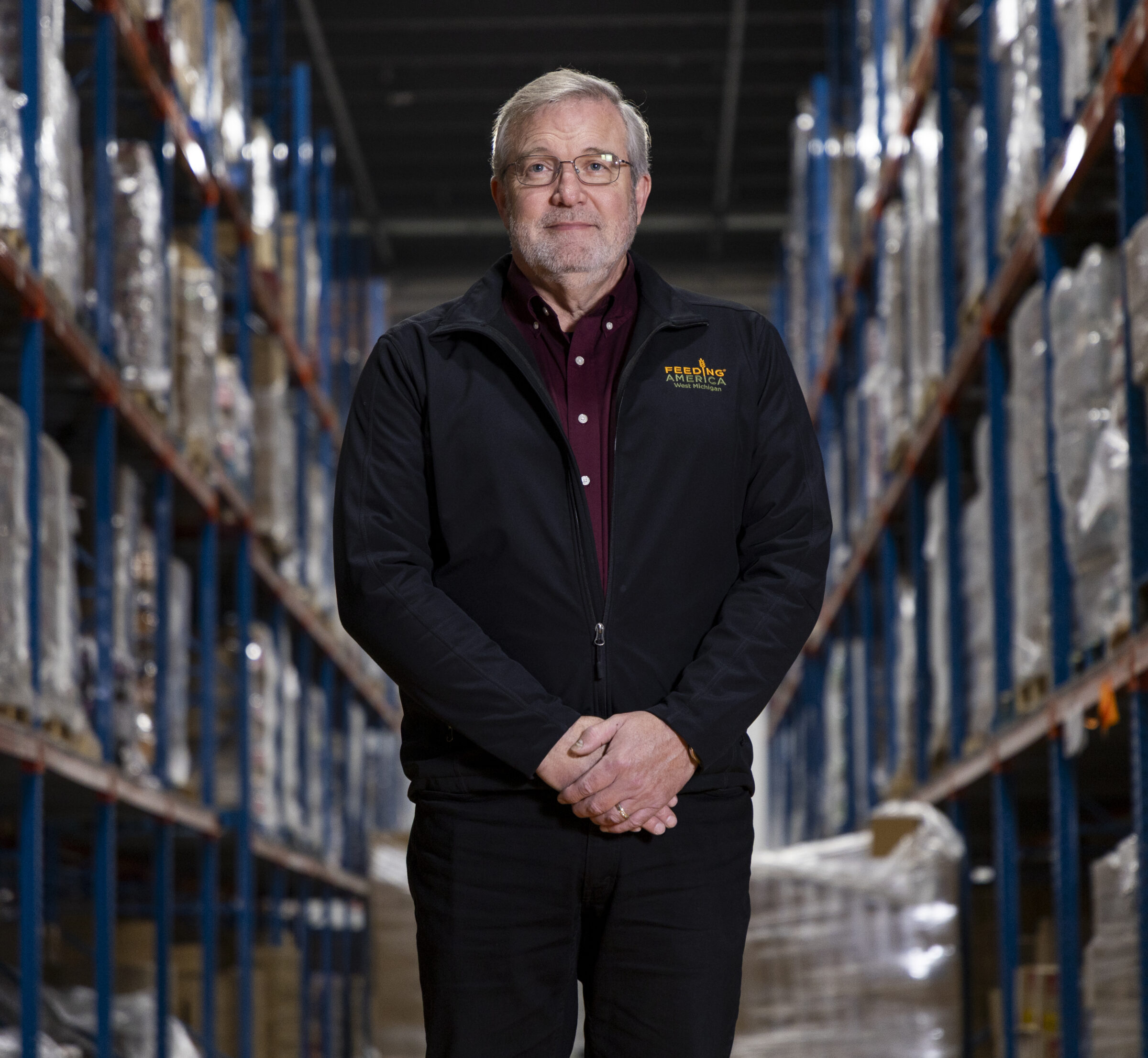 CEO and President of Feeding America West Michigan Ken Estelle standing in warehouse with full shelves. 