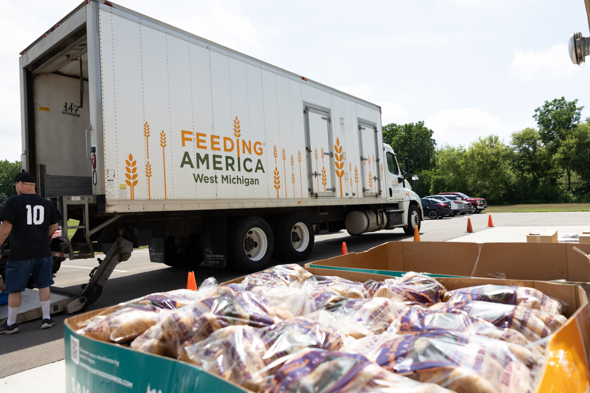 Feeding America West Michigan truck in background with a bin of bagged potatoes in foreground. 