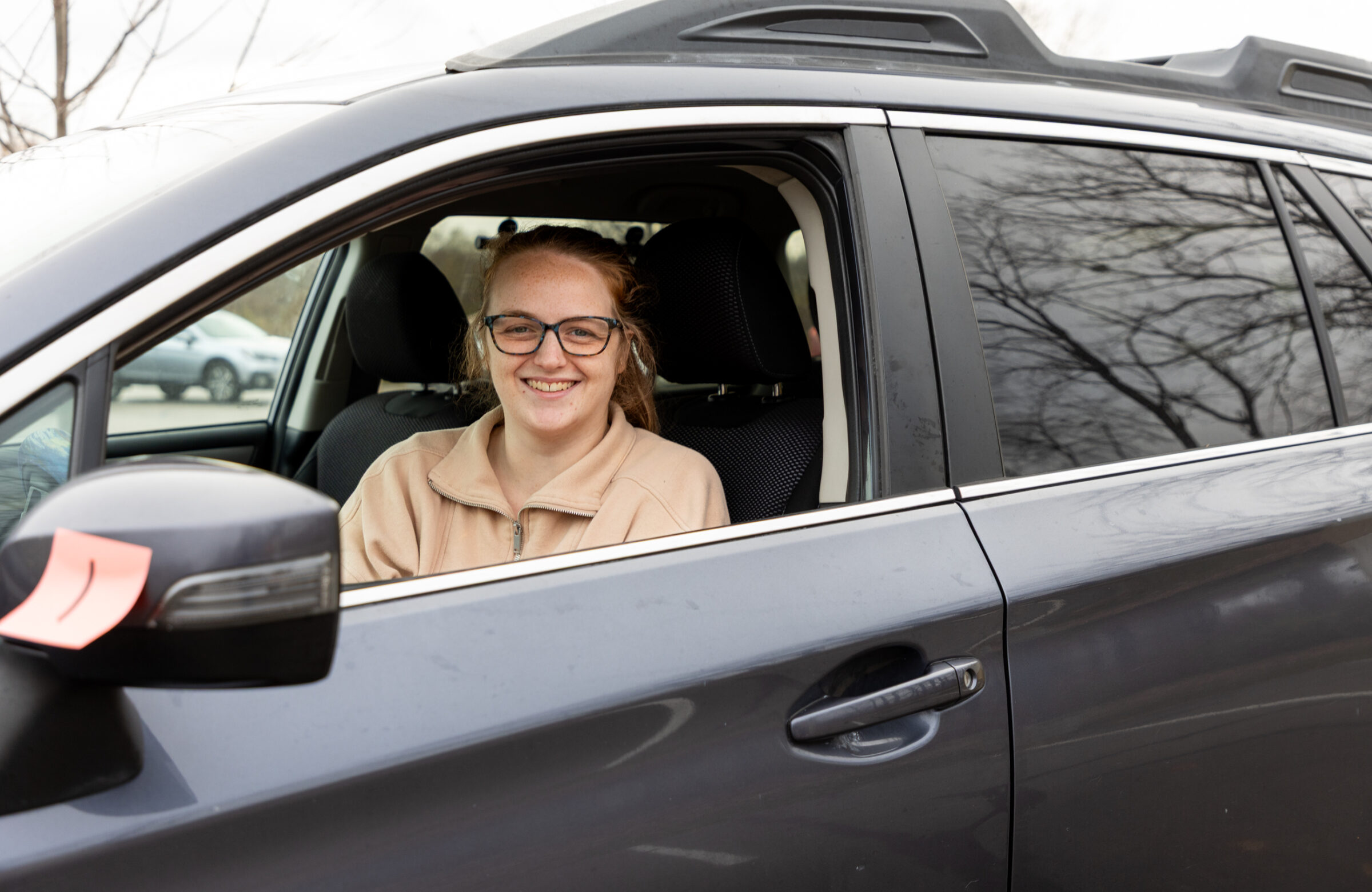 Woman wearing glasses sitting in her car and smiling. 