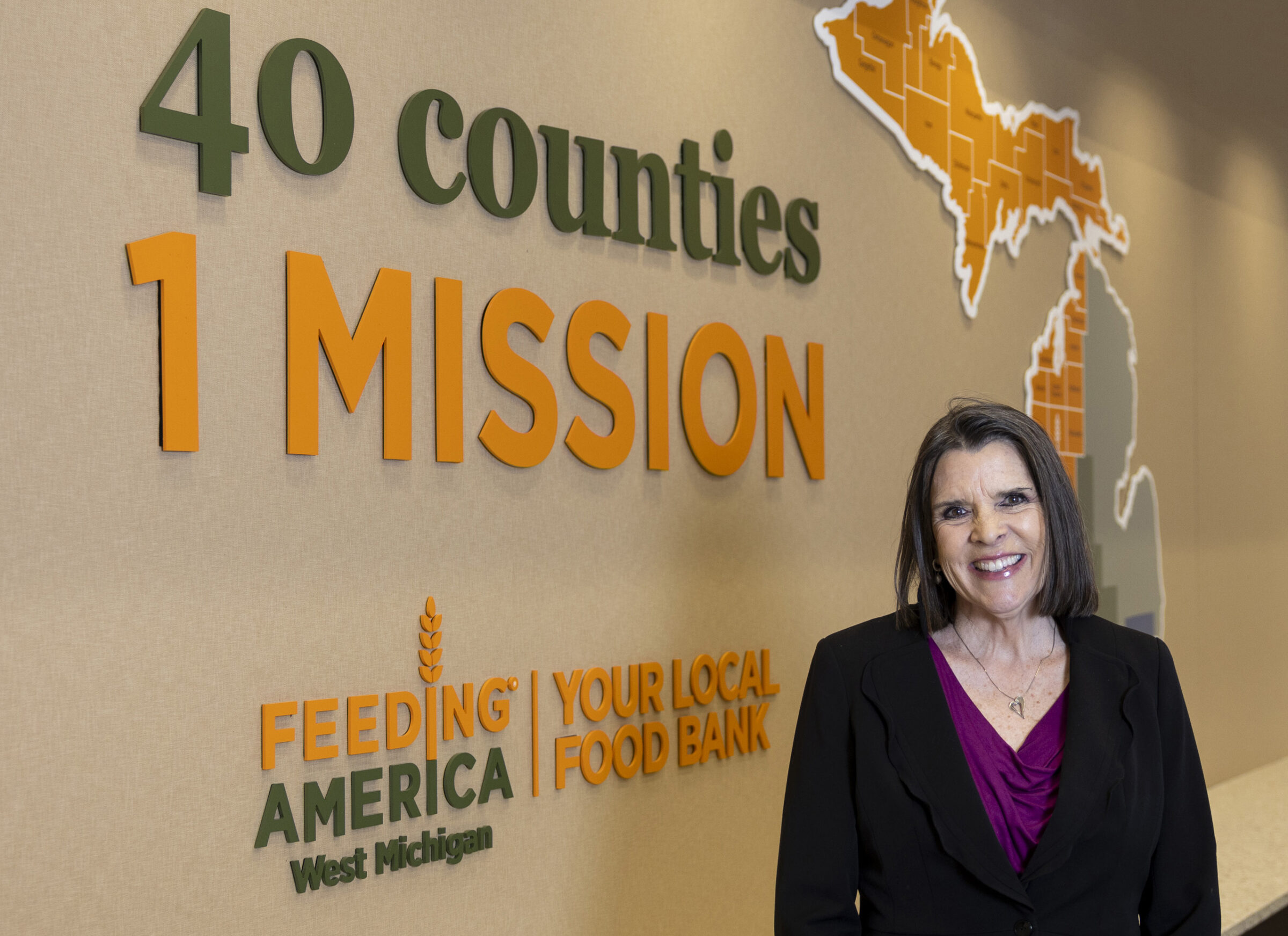 Feeding America West Michigan's new CEO Pattijean McCahill smiling and standing by a wall that says "40 counties, 1 mission". 