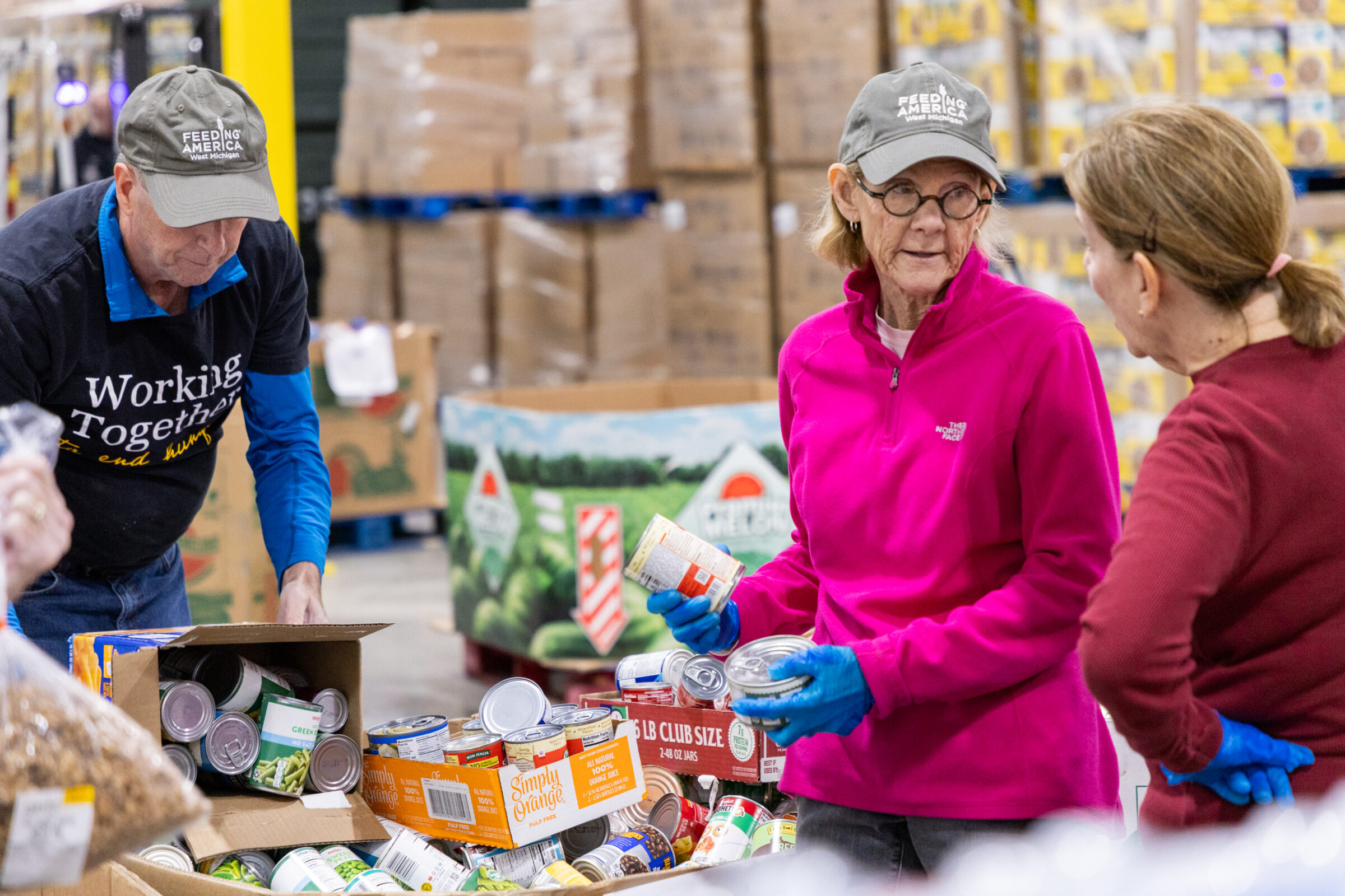 Tuesday regular volunteers at Feeding America West Michigan talking while packing boxes of food.
