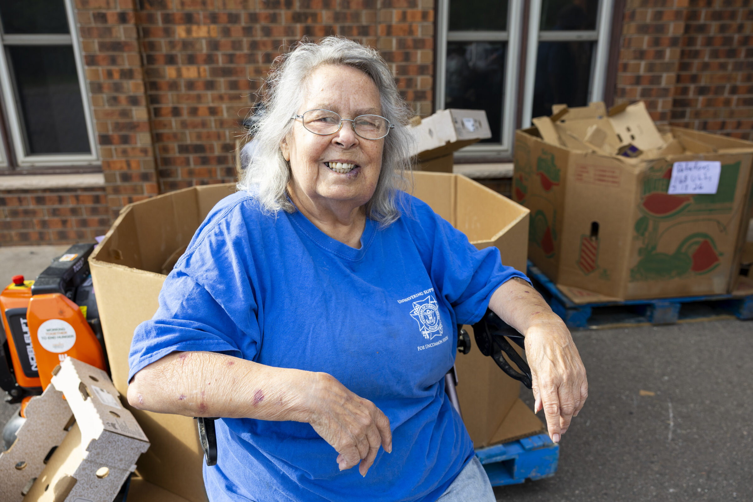 Mobile coordinator Annie smiling in front of large cardboard totes of food. 
