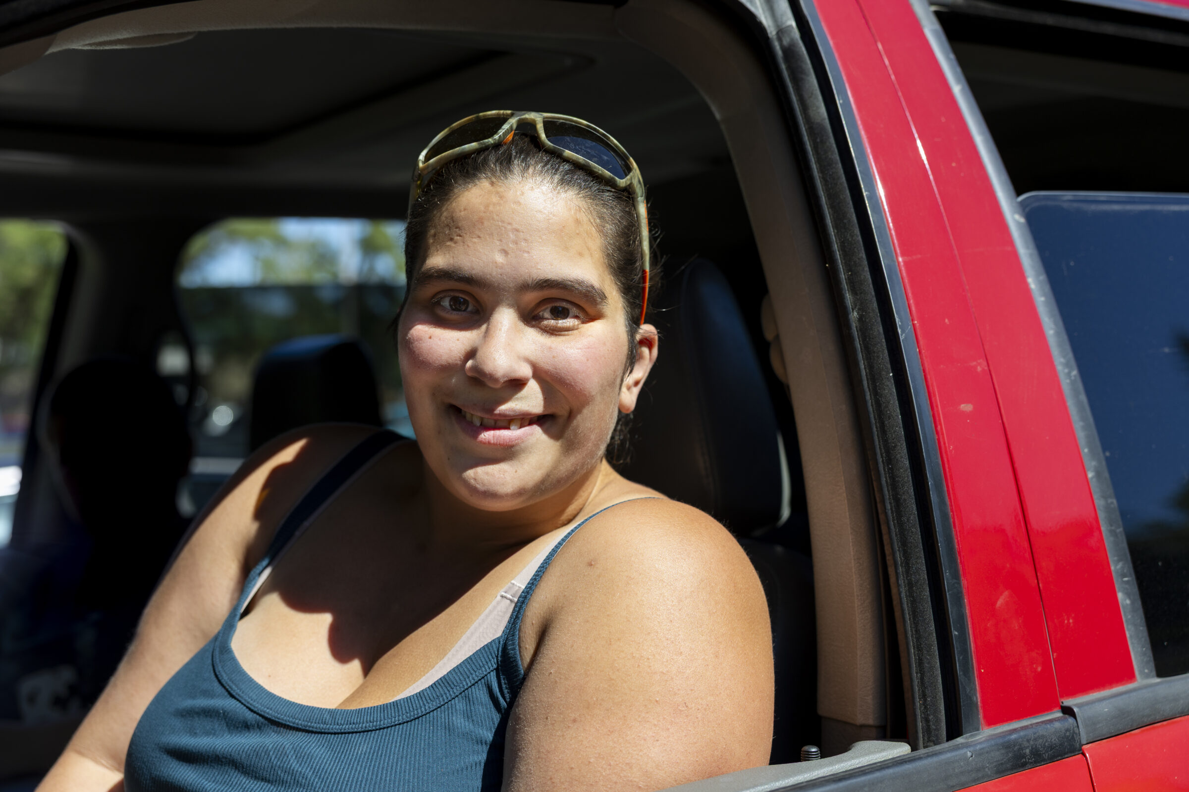 A smiling woman in her red car. 