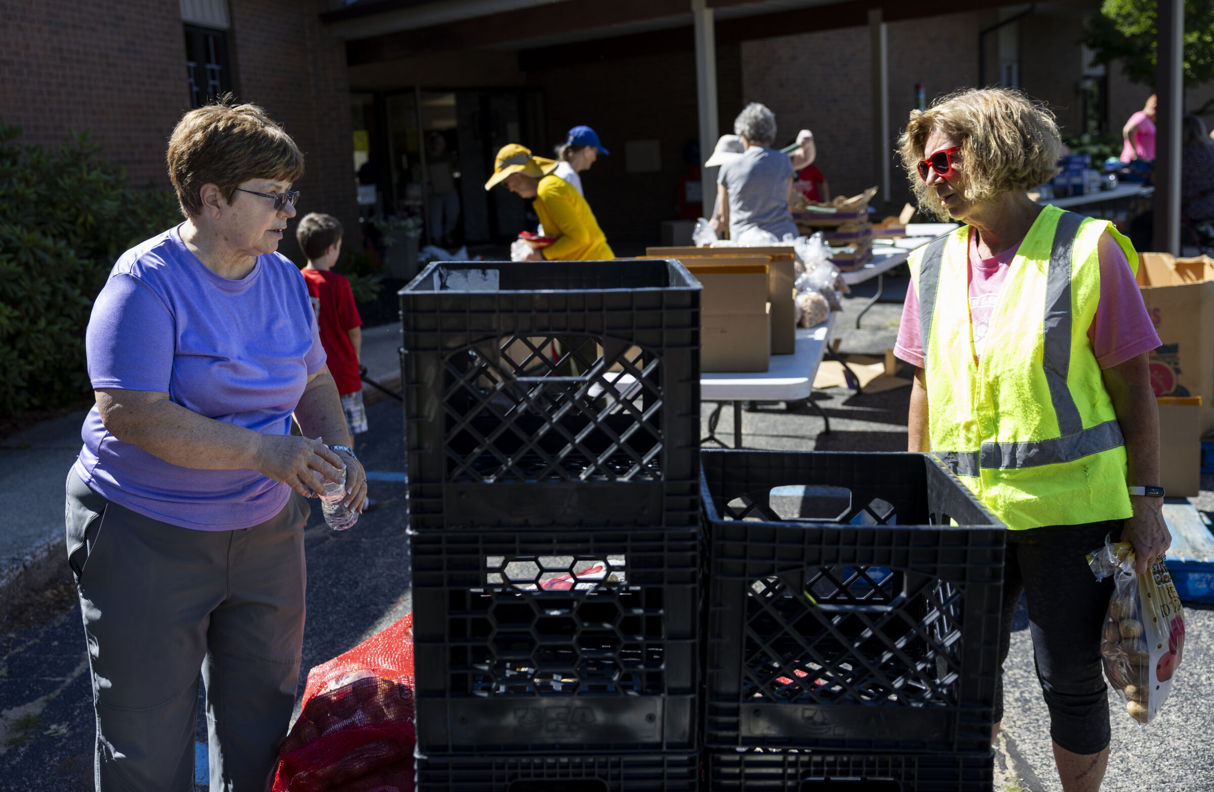 Two women standing across from one another. In between them are crates and tables with boxes. 