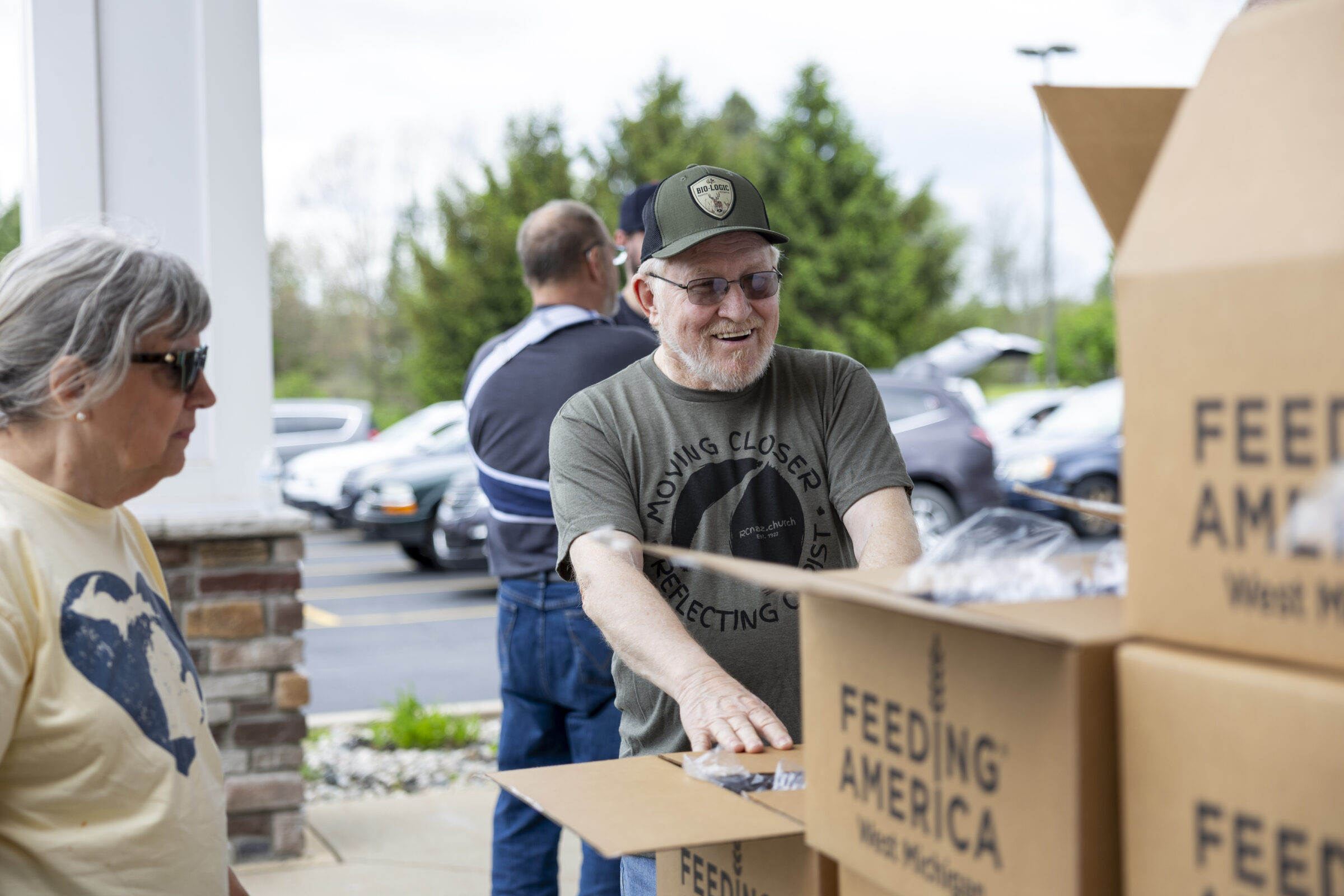 Site coordinator Ted smiles while talking with volunteers in front of several boxes of food for a mobile food pantry distribution.