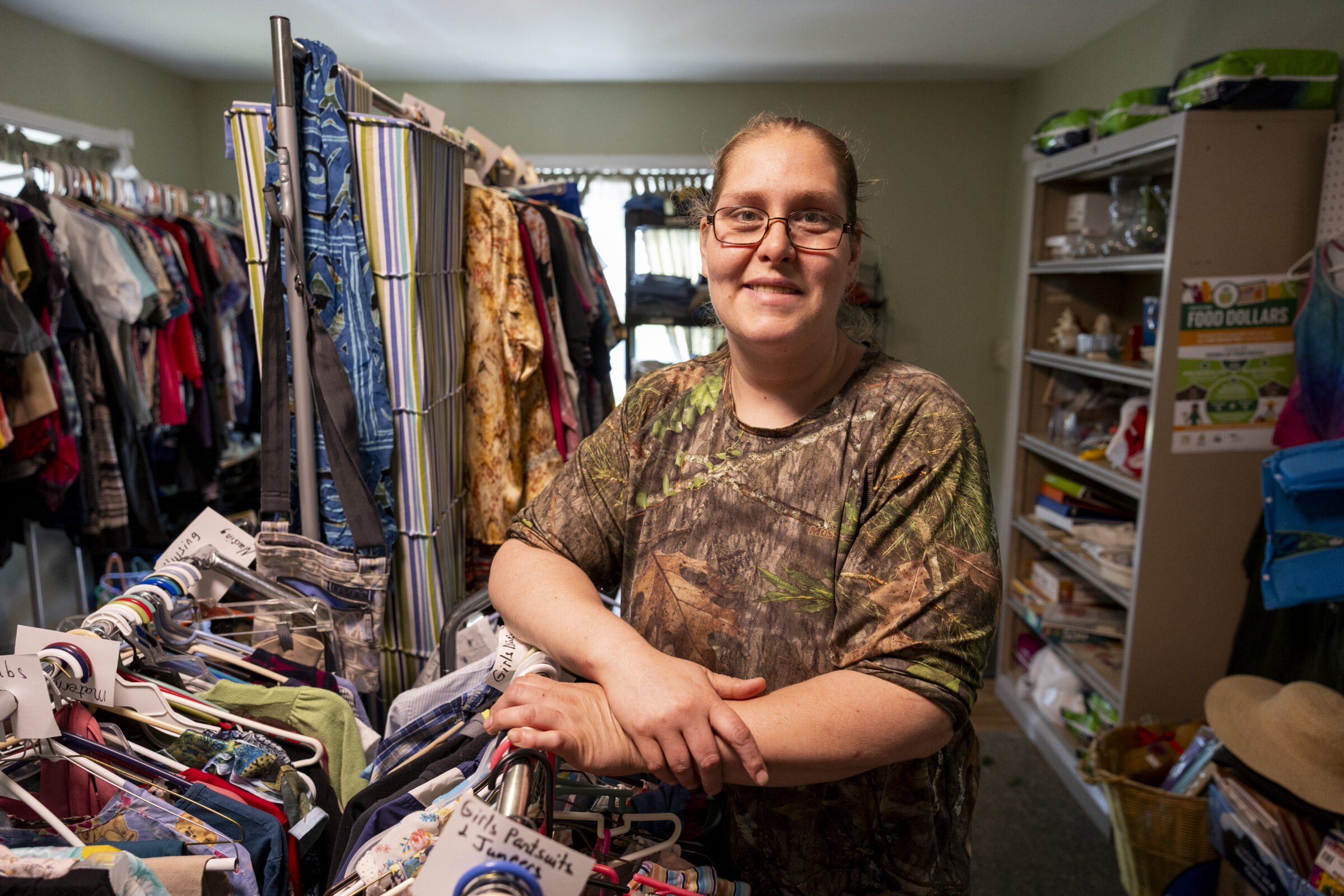 A woman smiling with standing next to a rack of labeled clothing.