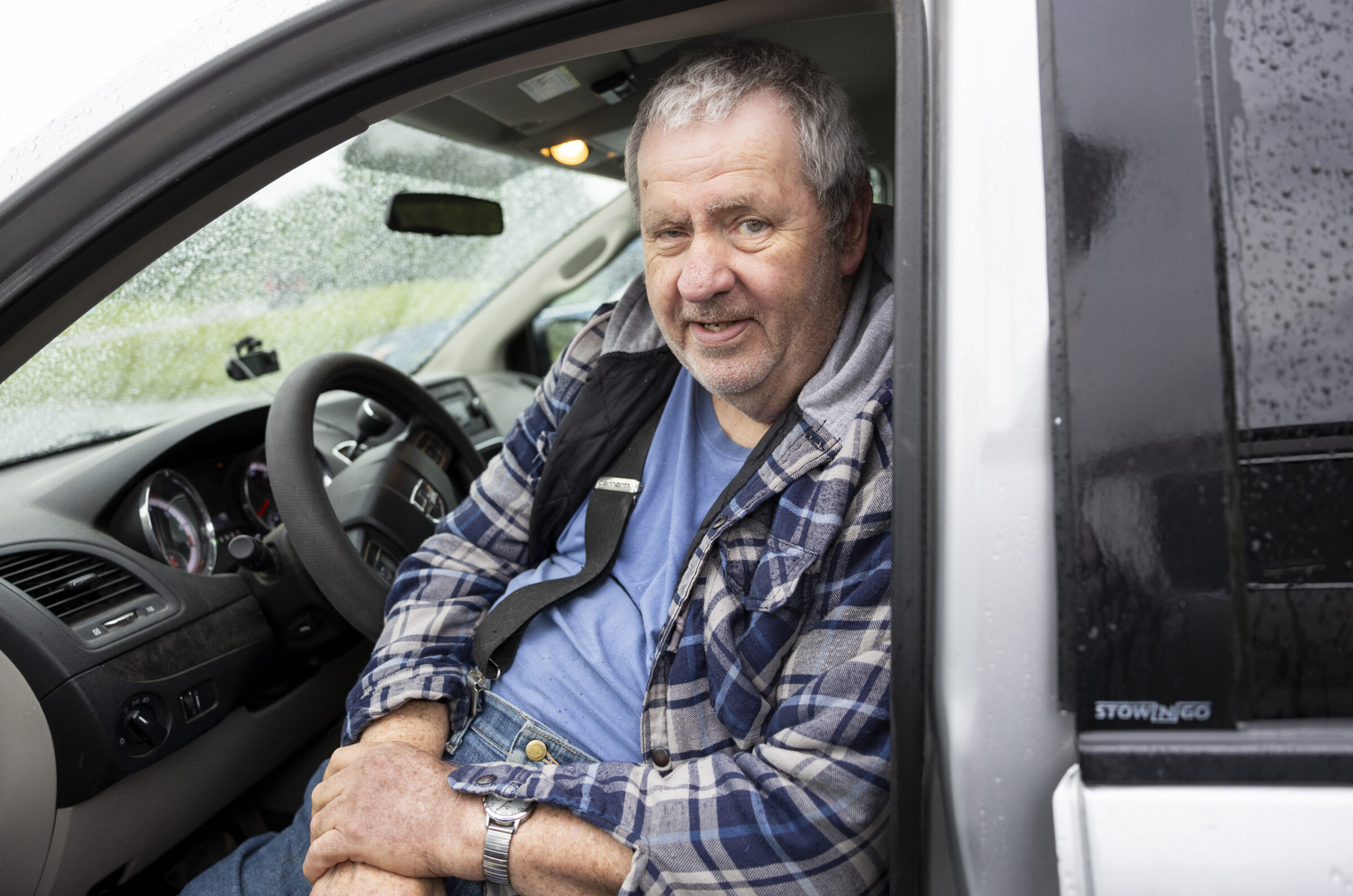 A man sitting in his car and looking out the open car door.