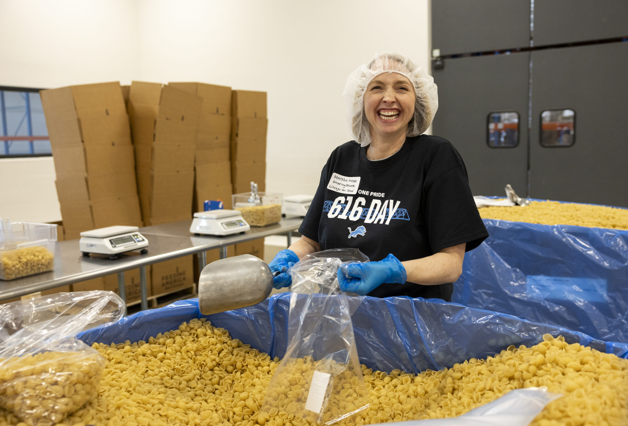 A woman standing behind a large cardboard tote of noodles, smiling.