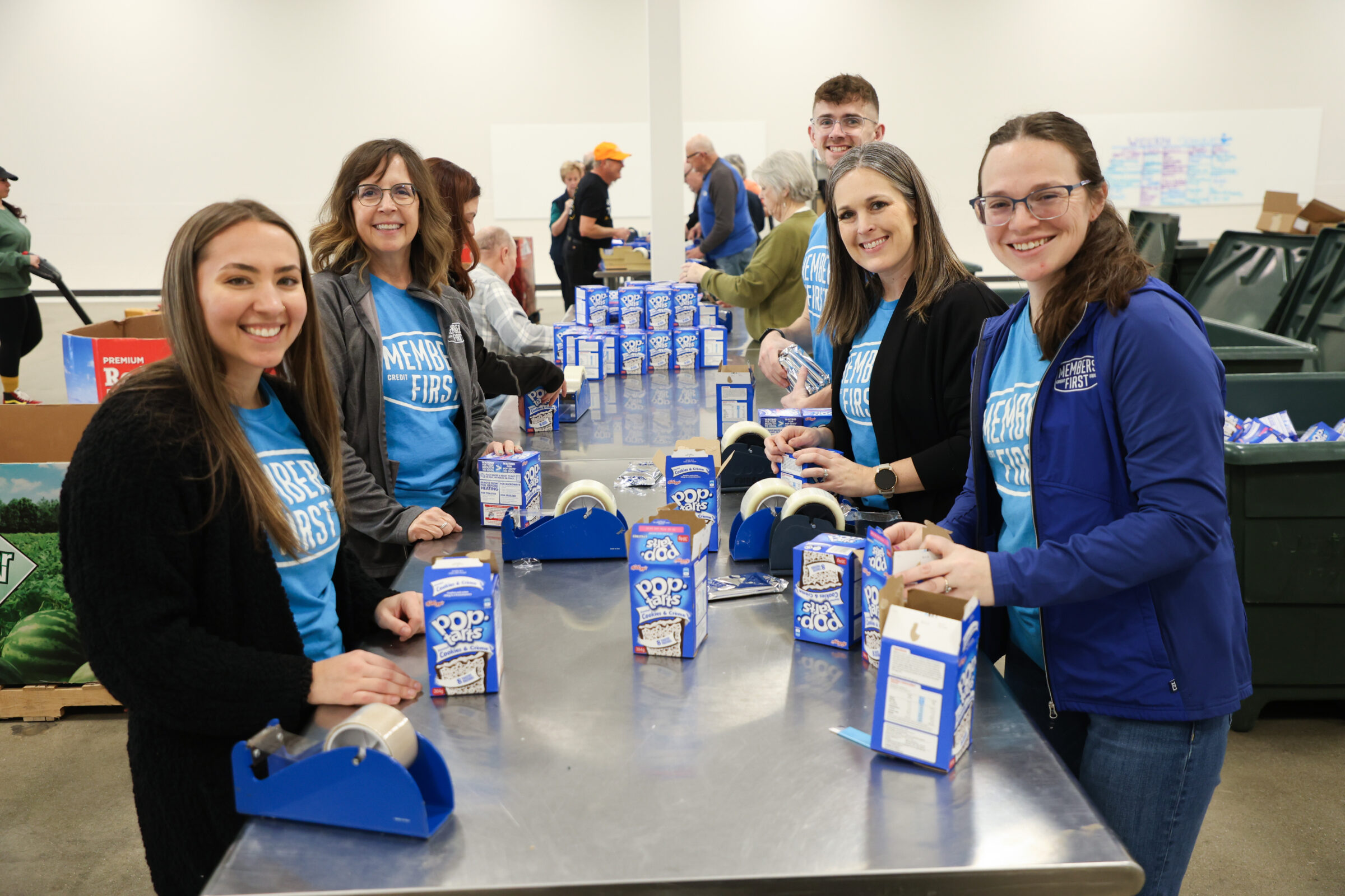 Volunteers standing on both sides of a large metal table. On the table are boxes of Poptarts.