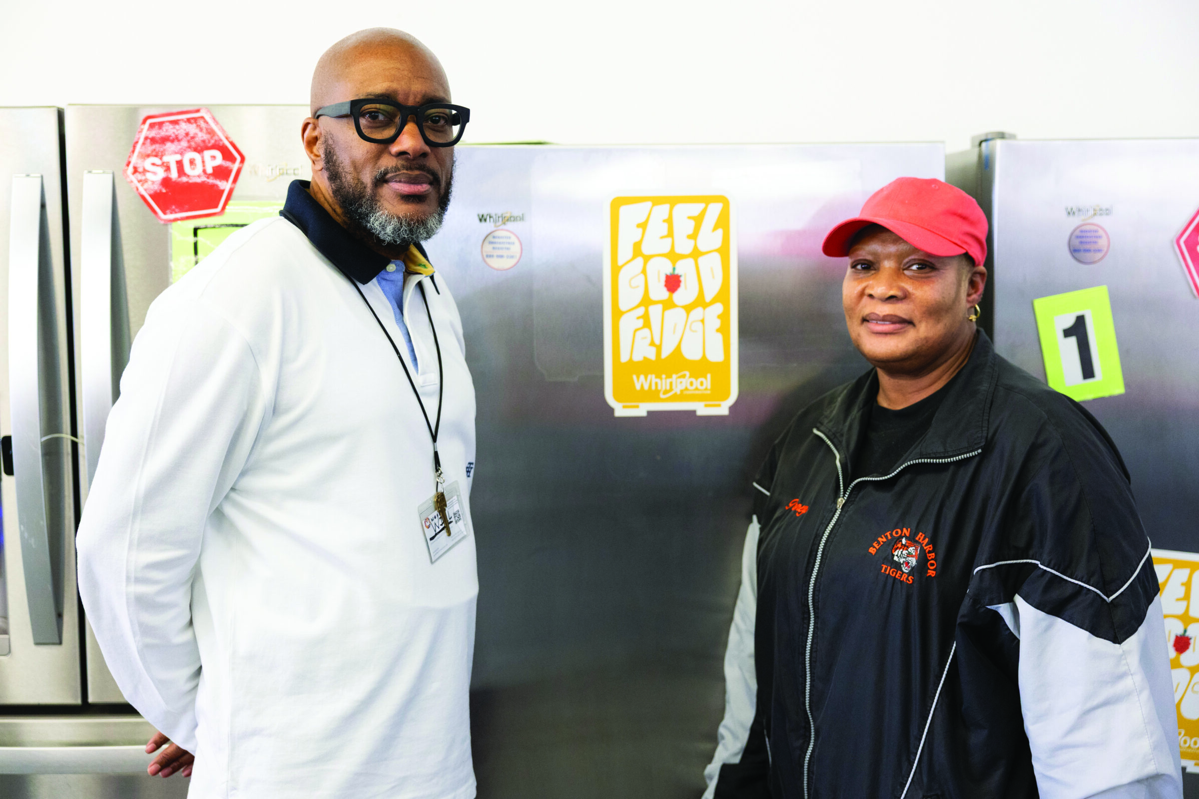 Pastor Gaddy stands left, and Feel Good Fridge coordinator Jimmyella stands right. Behind them are several stainless steel refrigerators.