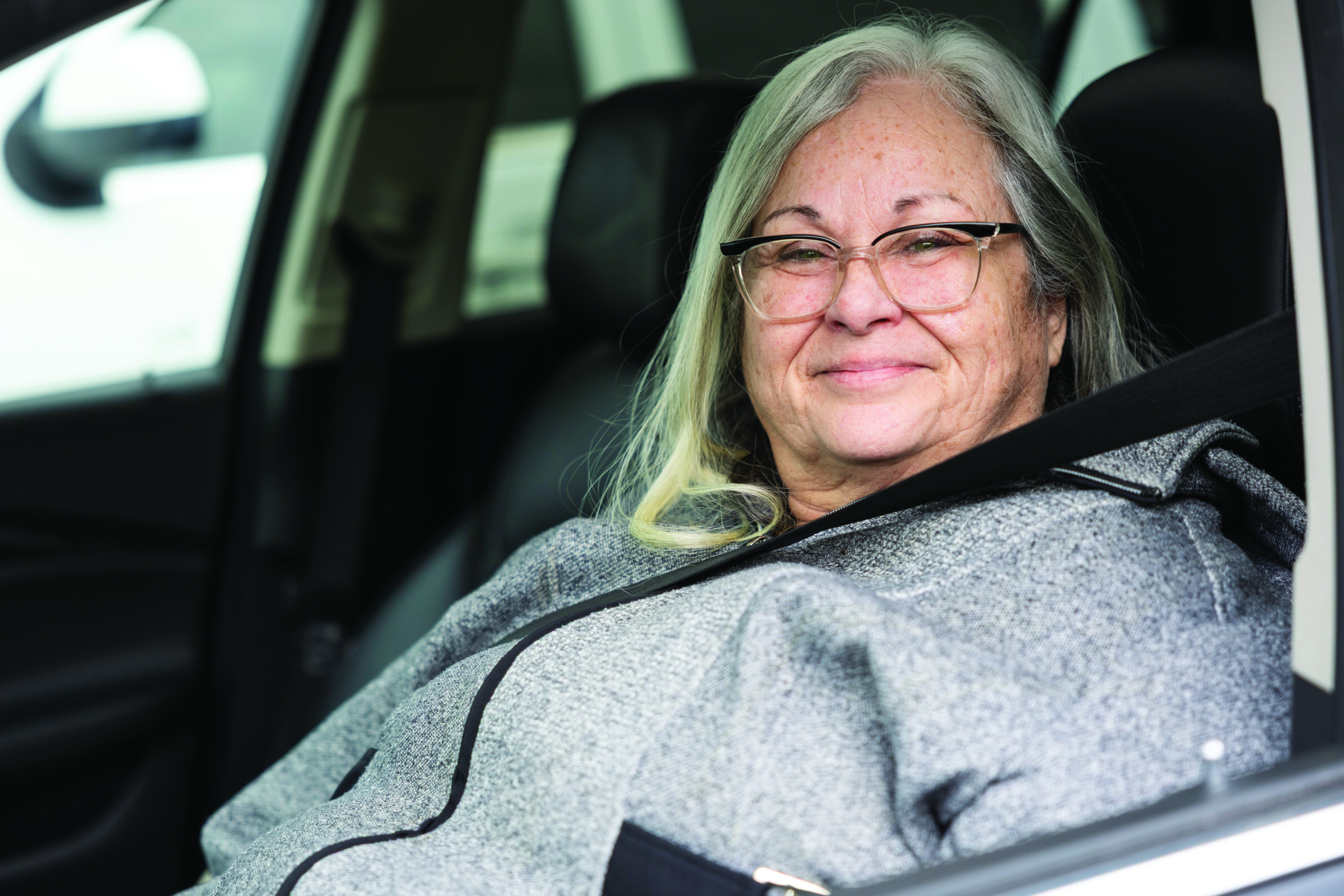 A smiling woman sitting in her car.