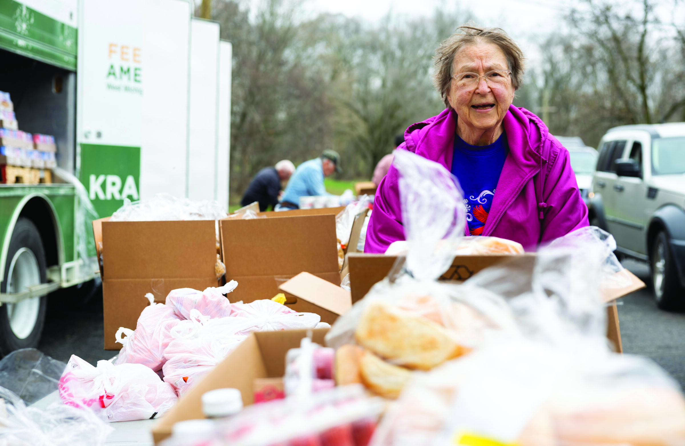 Mobile coordinator Susie stands at the end of a table filled with bagged food items.